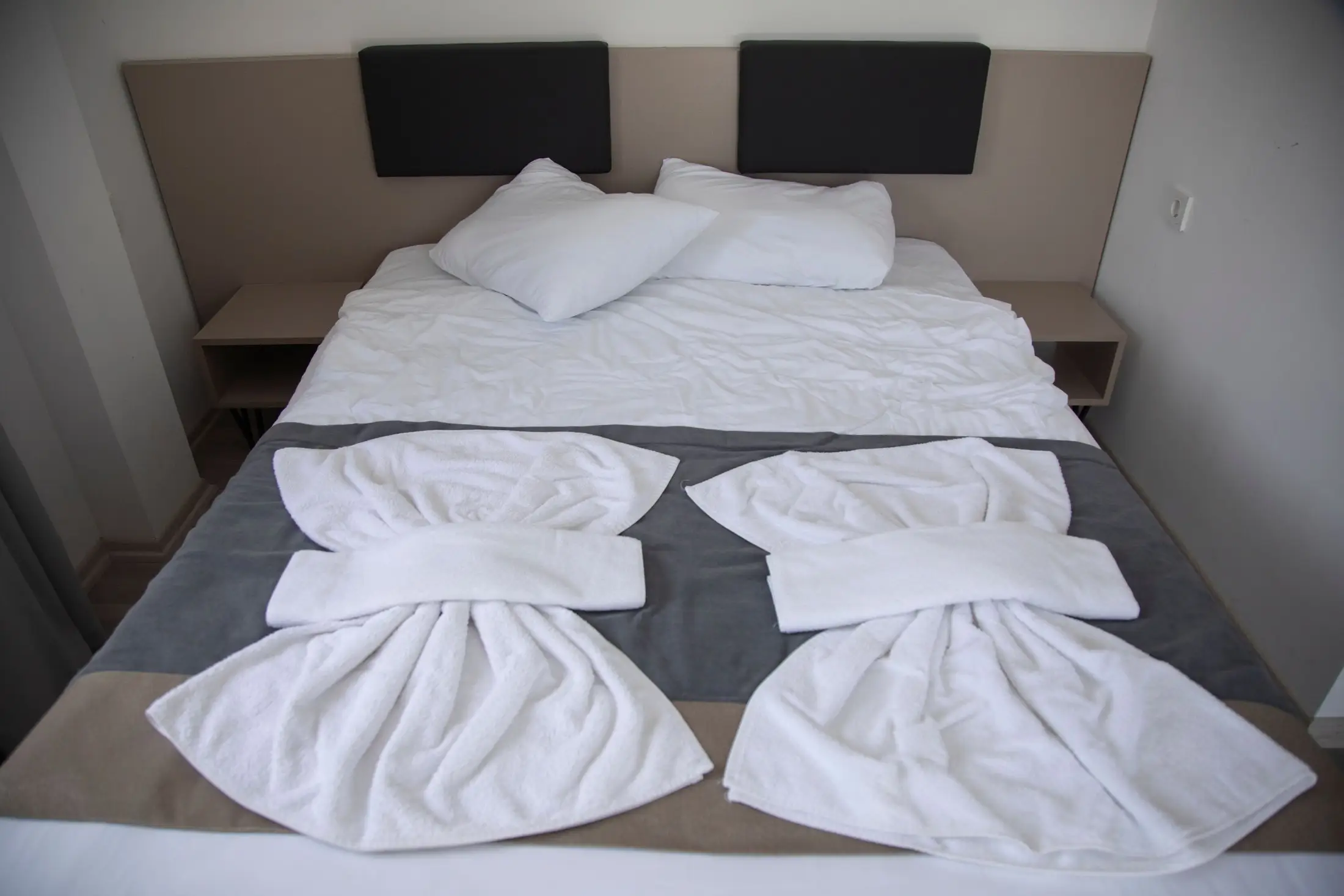 Lit double aux draps blancs, avec deux serviettes pliées posées sur un chemin de lit gris