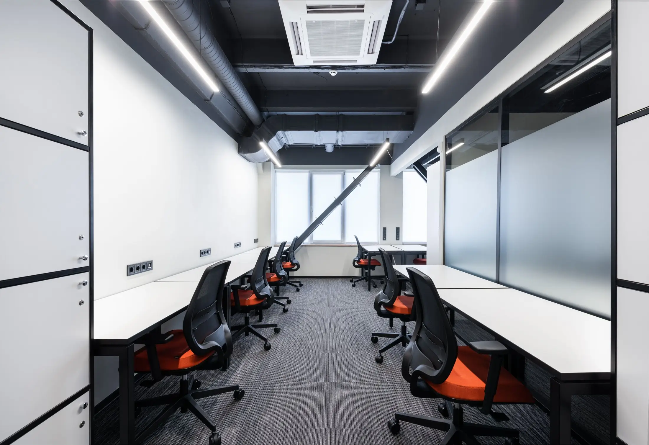 Open space vide avec bureaux blancs alignés, chaises orange et moquette grise