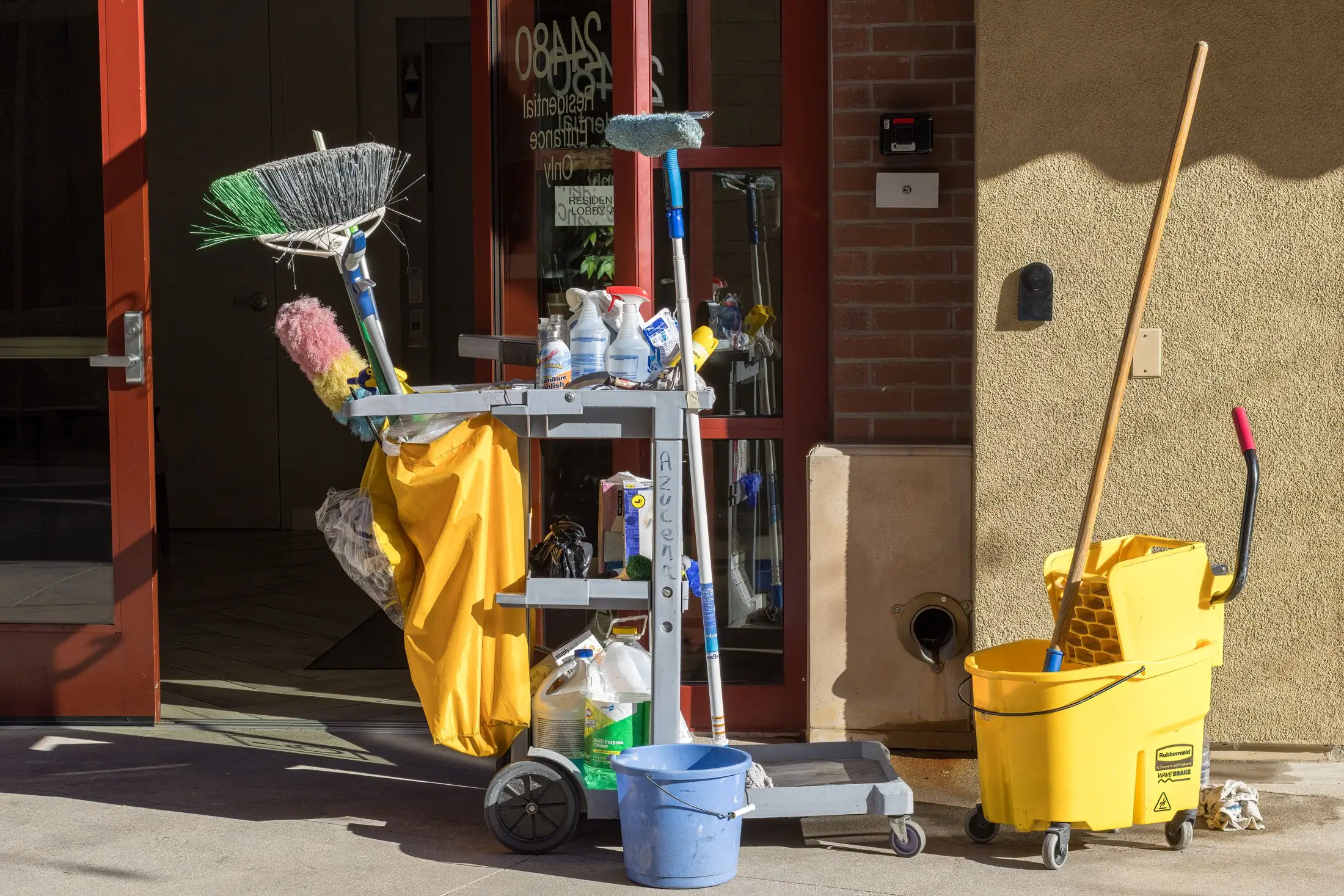 Chariot de nettoyage chargé de balais, de vaporisateurs et de sacs, à côté d'un seau jaune à essoreur