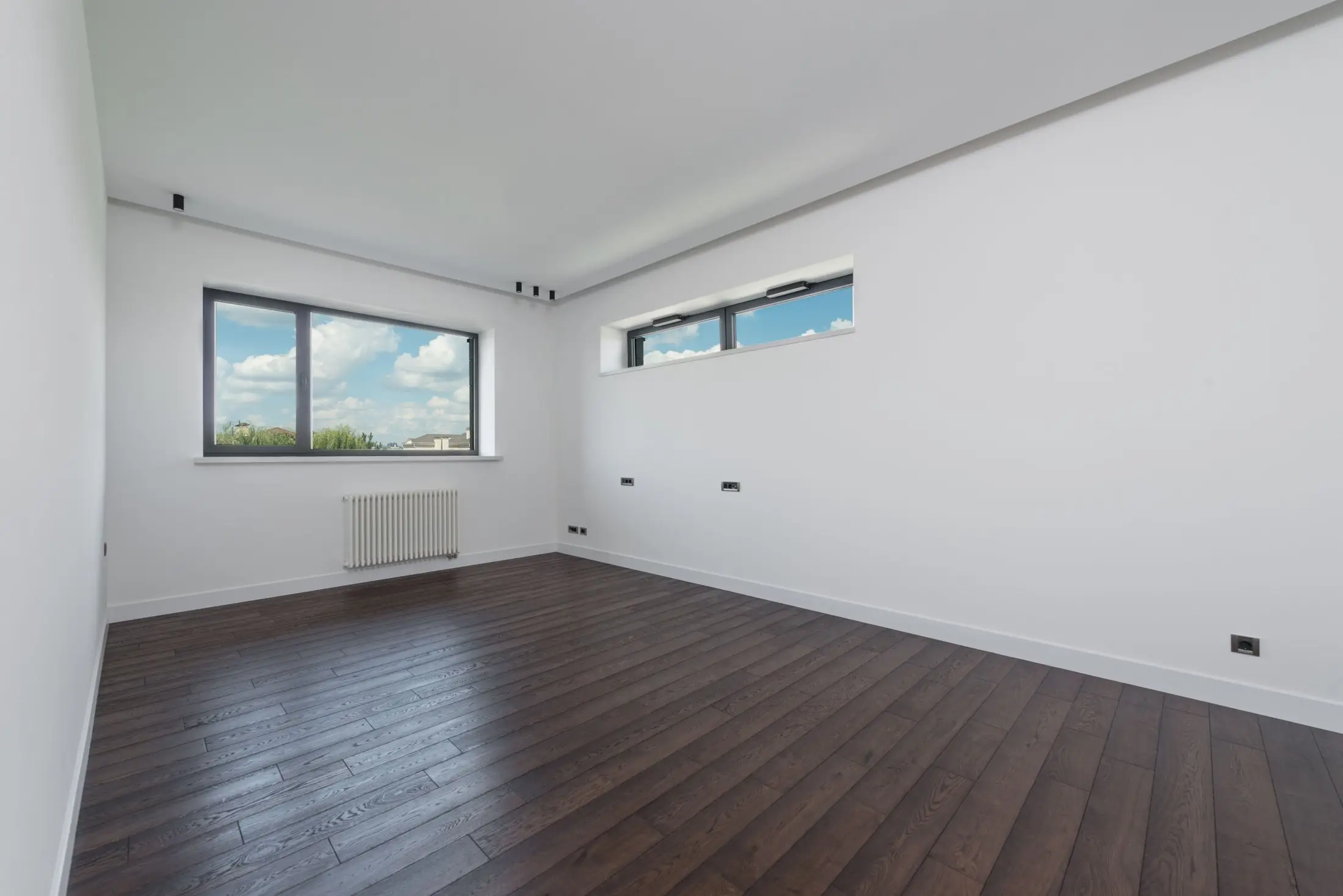 Pièce vide fraîchement rénovée, murs blancs, parquet foncé et fenêtres ouvertes sur un ciel bleu