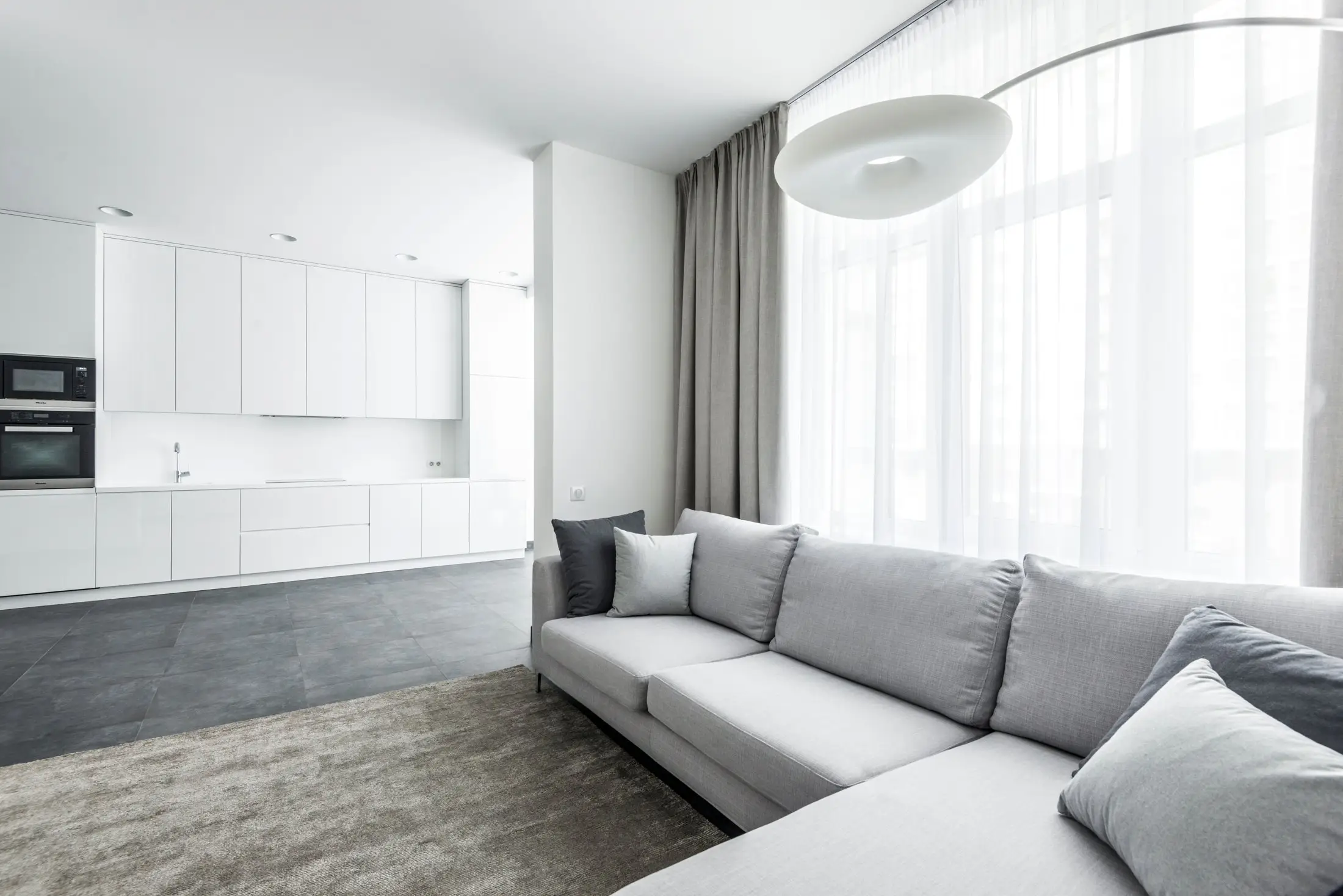 Canapé d'angle gris clair posé sur un tapis dans un salon lumineux
